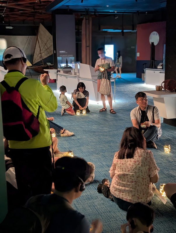 在「燈與詩的夜間導覽」活動中,導覽員邀請觀眾們席地而坐一面讀詩,一面透過展覽來反思詩句帶著人們的提醒。(穀雨企業社提供照片)