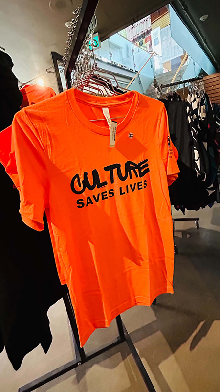 出現在 SLCC賣店的橘色T 恤，上頭寫著「Culture Saves Lives（文化拯救生命）」。